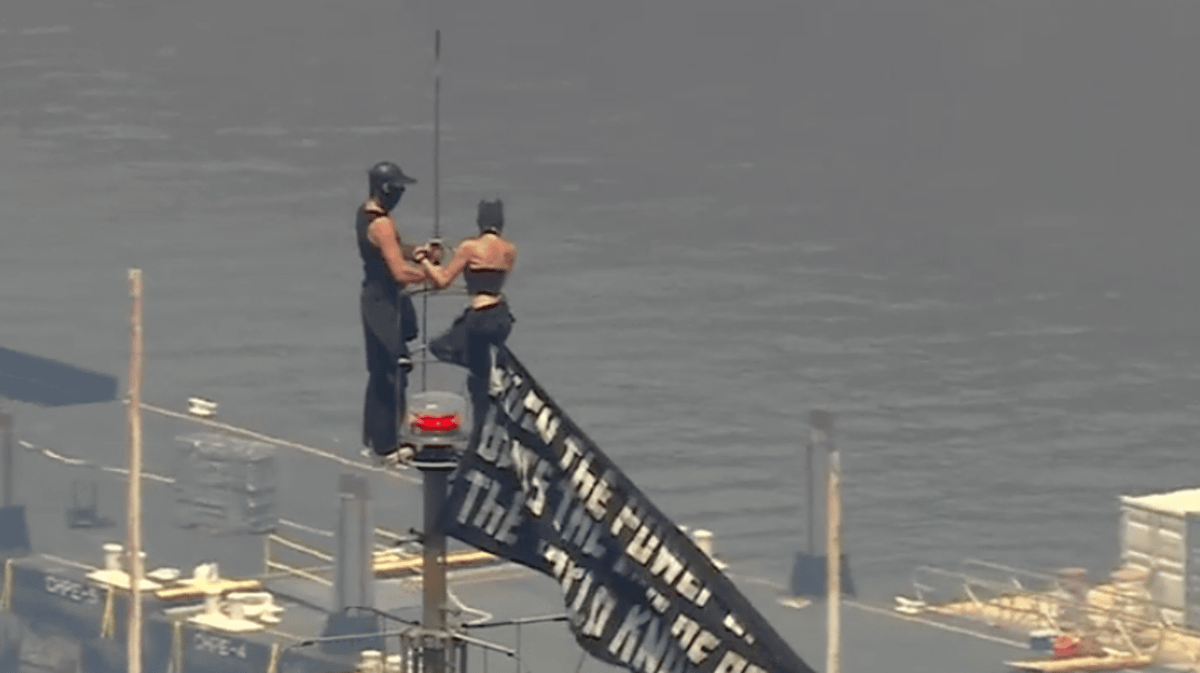 Two individuals climb on high of the Empire State Constructing with message on banner